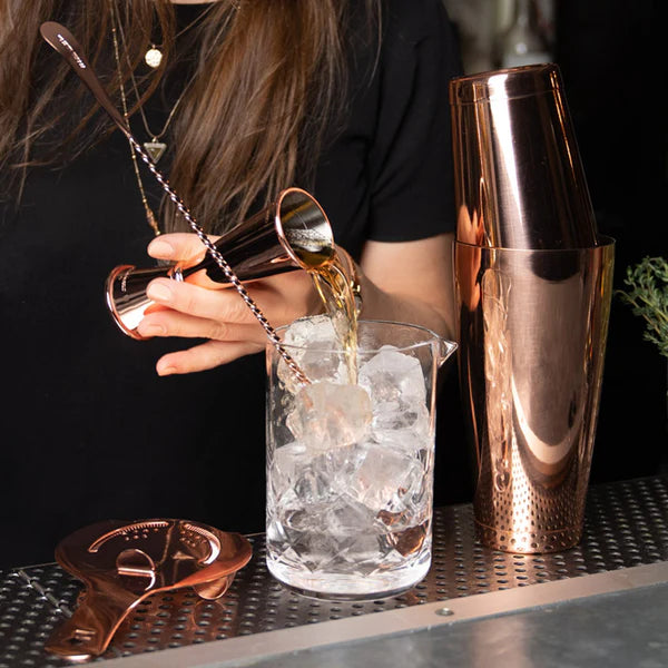1121 C Cocktail Kingdom Koriko Set of 2 Weighted Tins in copper shown mixing cocktail, with copper Stainer, mixing spoon, jigger and glass on bar top.