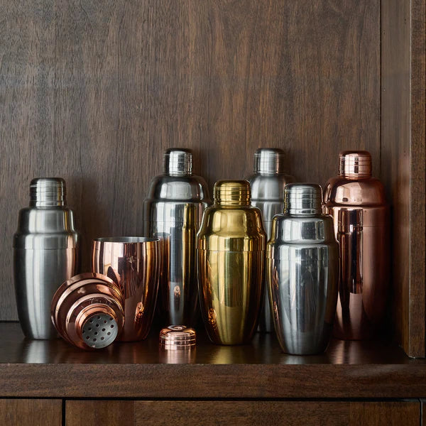 Various cocktail kingdom shakers in various colors shown on wooden background.