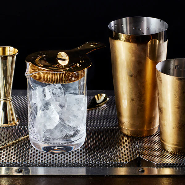 1126_G_Cocktail Kingdom Koriko Hawthorne Strainer shown with gold shakers, jigger and mixing spoon on bar top. 