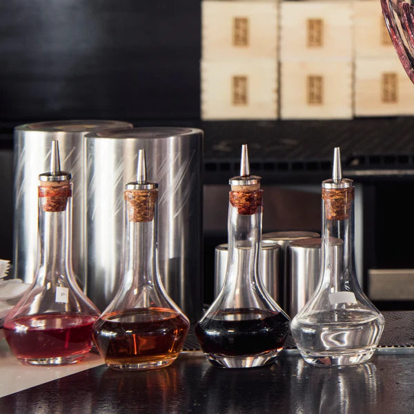 1137_Cocktail Kingdom Plain Bitters Bottles with Cork Dasher shown in bar setting with dark background.