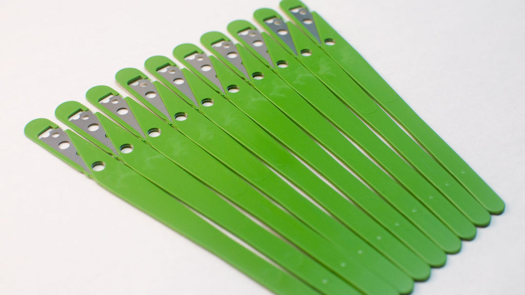 10 green bread lame blades with the protectors still on splayed out next to each other