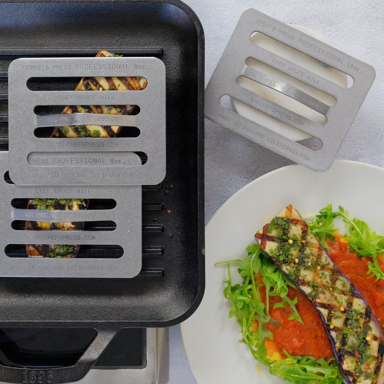 Two Chef presses on Grilled vegetables next to a plate of food with a gray background