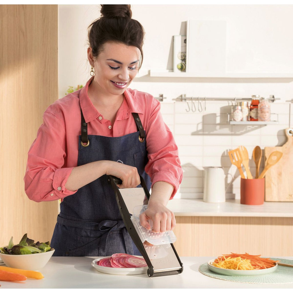 Woman in a kitchen using a mandoline slicer to cut vegetables.