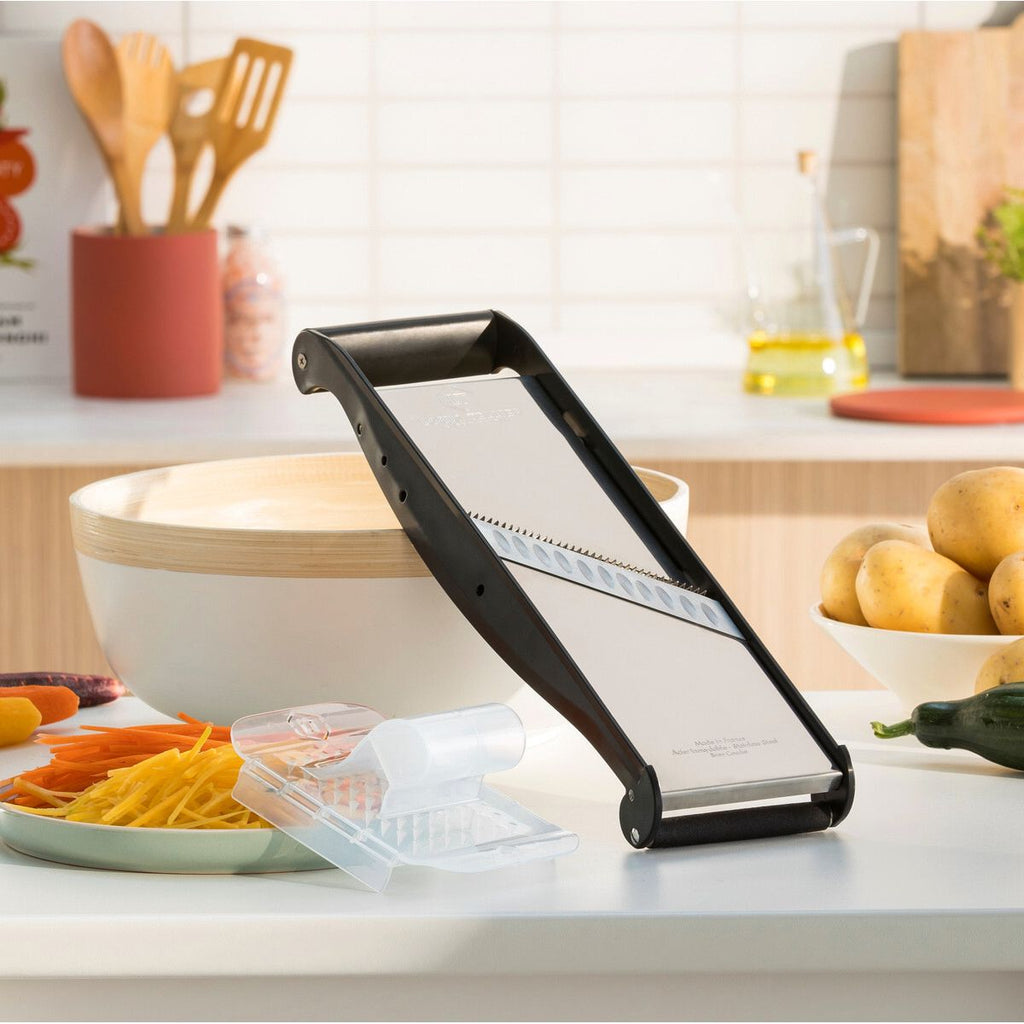Vegetable slicer on a kitchen counter with sliced vegetables and a bowl in the background