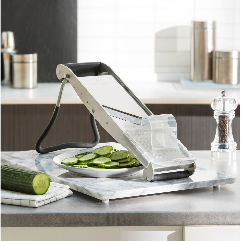 Mandolin slicing cucumber on a kitchen counter with a pepper grinder.