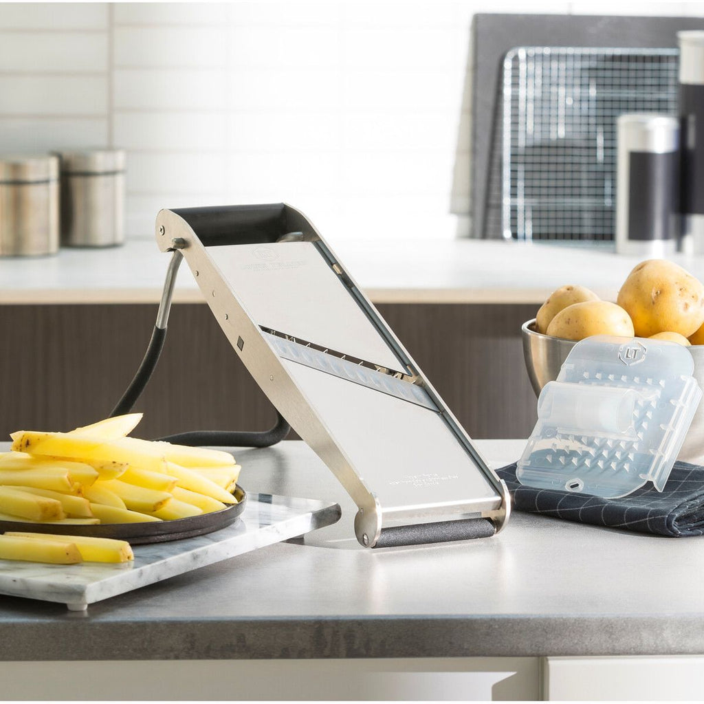 Professional kitchen Mandolin on a kitchen counter with bananas and a bowl of fruit in the background.