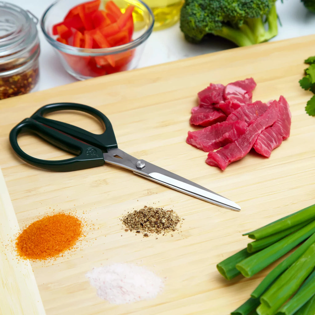 Joyce Chen Scissors in dark olive shown on cutting board with meats and vegetables.