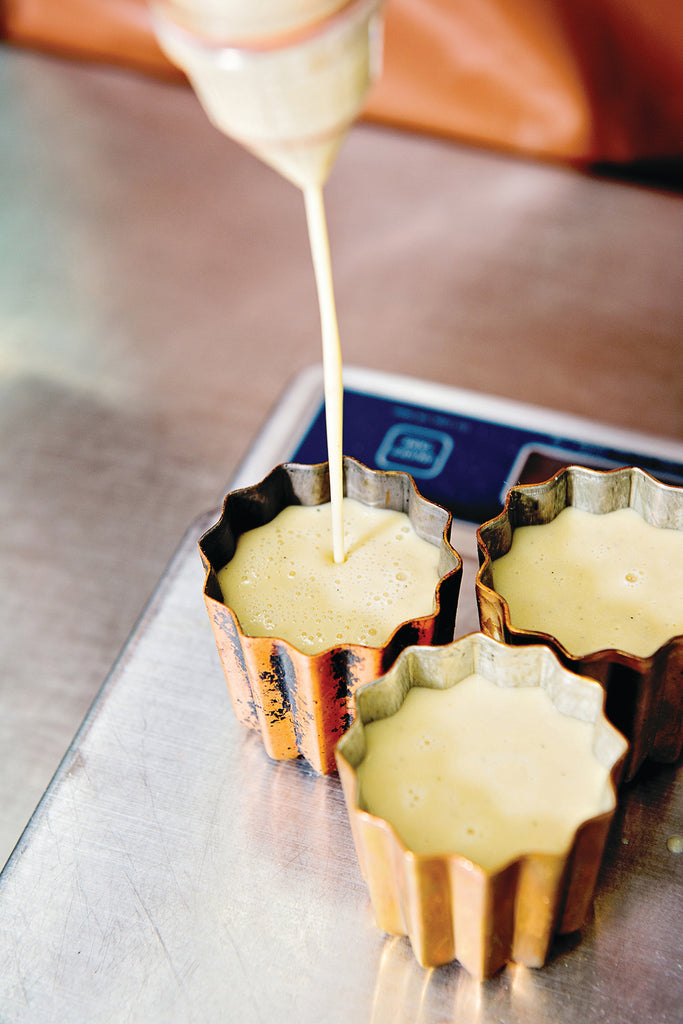 pouring of pastry filling into a copper colored tin mold on metallic surface. 