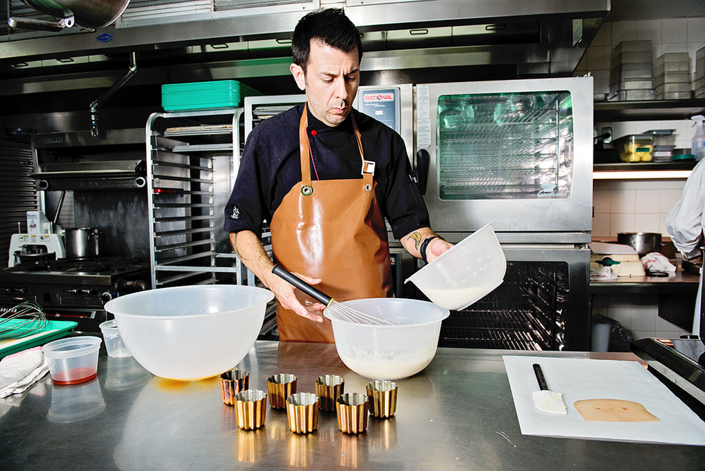 Chef in a kitchen preparing food with various utensils and and copper colored tin molds.