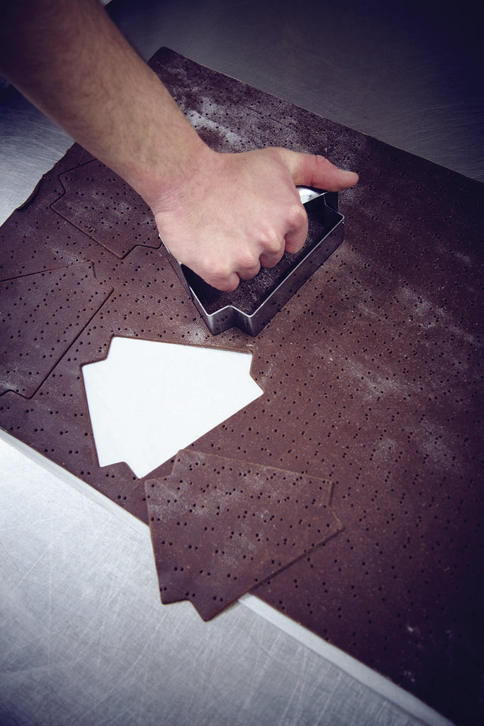 Hand using a triangular tart mold to cut out a piece of chocolate on a metalic table.