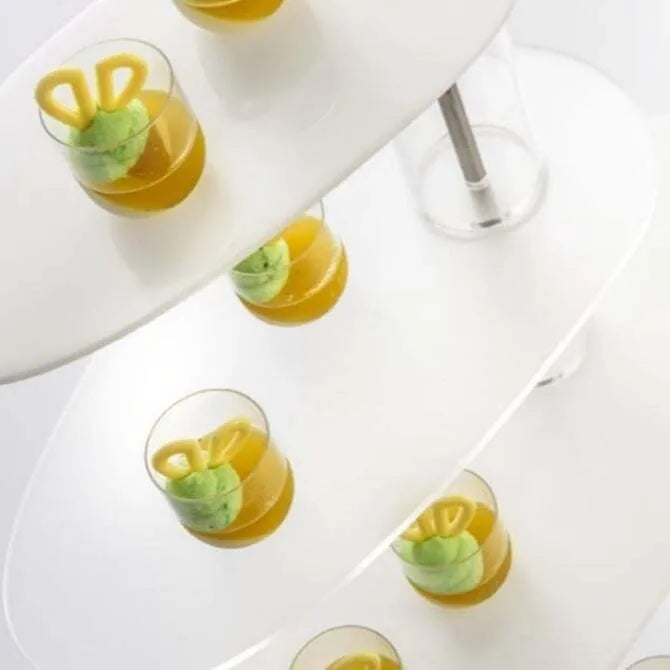 Several Plastic Tumblers filled with yellow pastry confections shot from an overhead point of view on a white multi level serving tower.