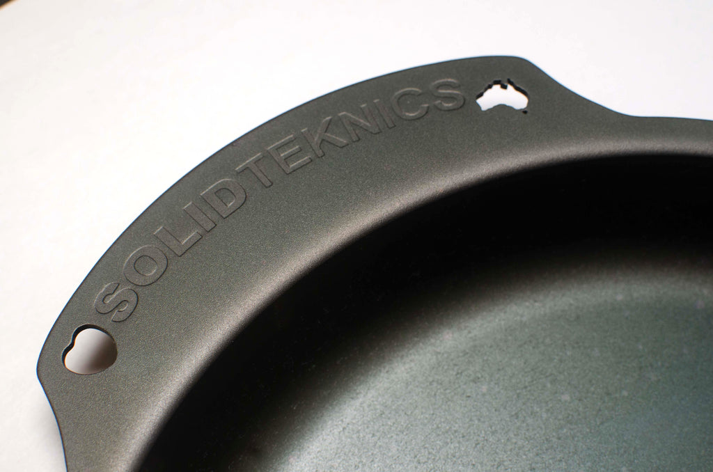 The handle of a seasoned black carbon steel skillet on a white background