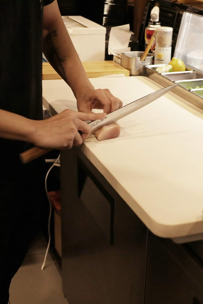 Sushi being cut on beige cutting board by chef knife.