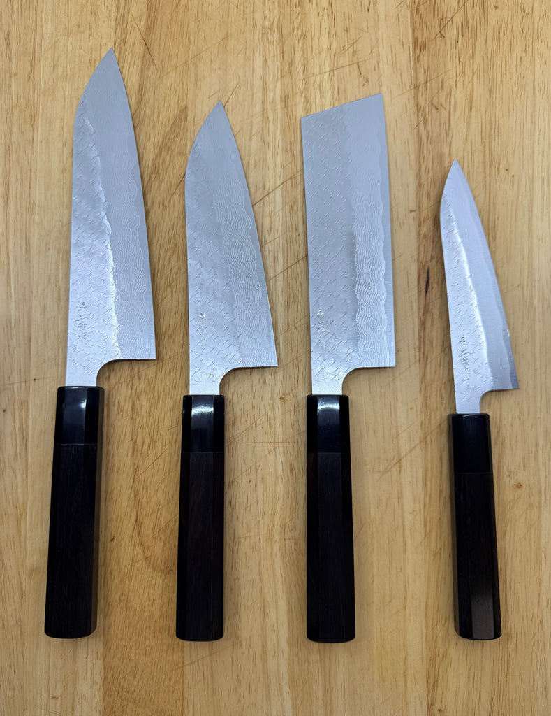 Four Nigara chef's knives with black ebony handles on a wooden surface.