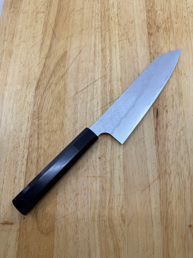 Nigara SG Strix Gyuto 210mm with black ebony handle laying down on brown wooden cutting board. 