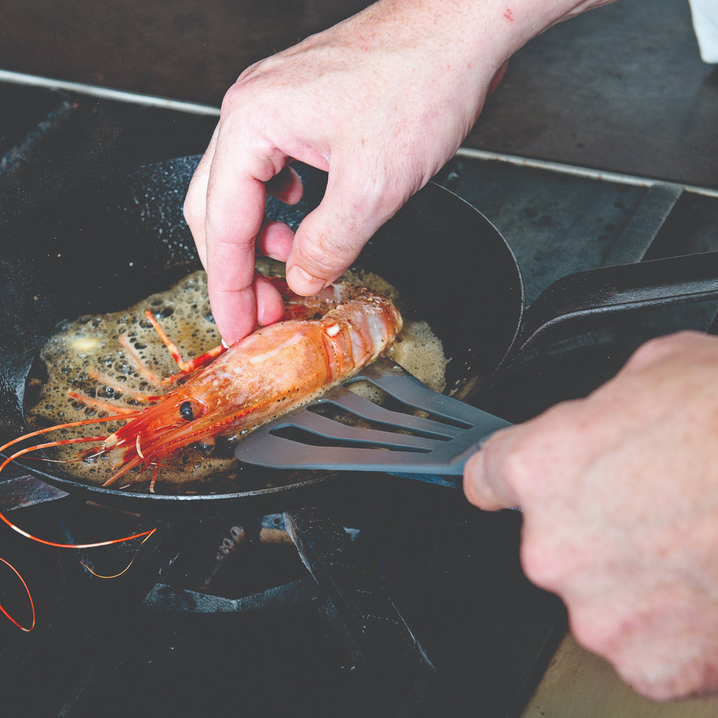 Person cooking a prawn in a pan with a grey slotted spatula