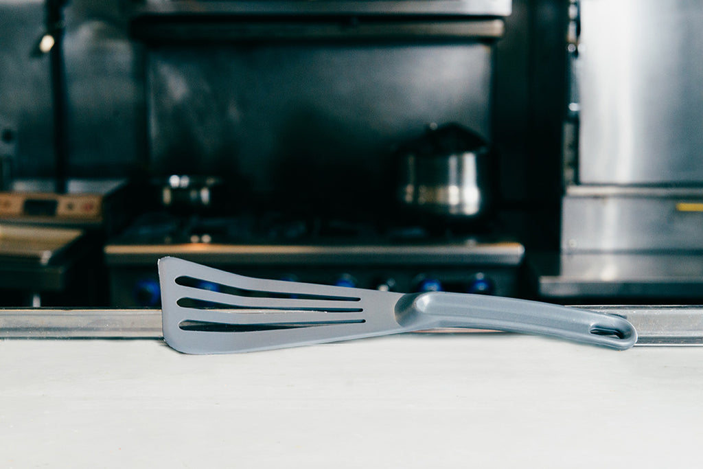 Grey spatula on a white kitchen counter with a blurred stove in the background
